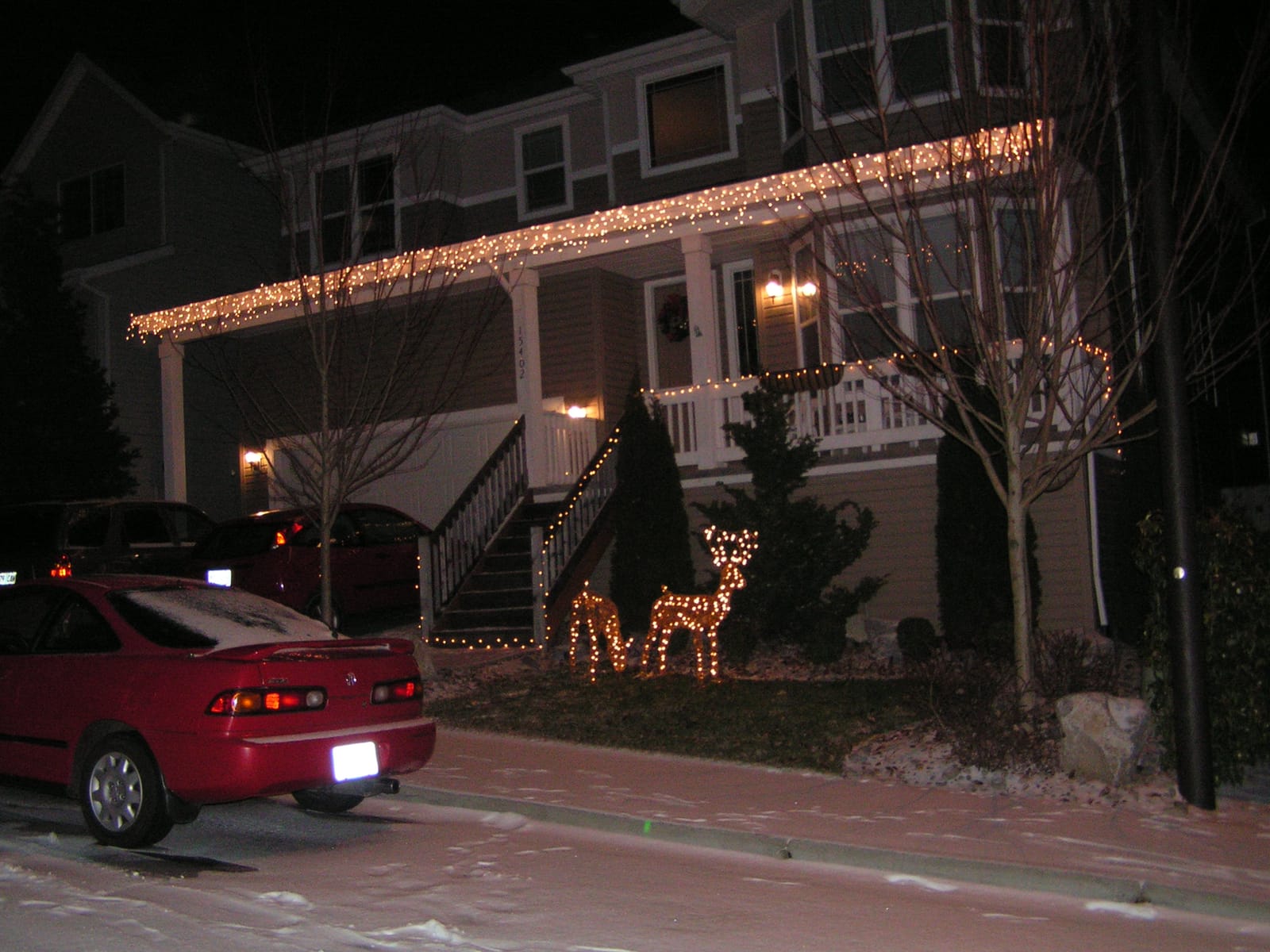House decorated with Christmas lights and lit-up reindeer lawn ornaments at night, with snow on the ground