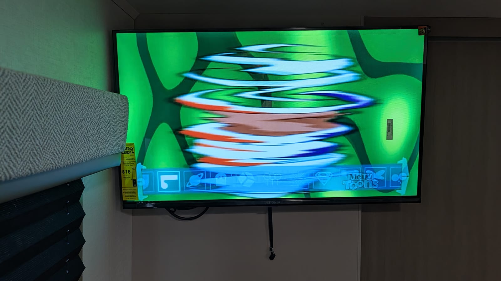 The TV seen straight on, showing a fast-moving cartoon blurred into streaks of white, orange and blue on a green background, with the MeTV Toons logo at the bottom.