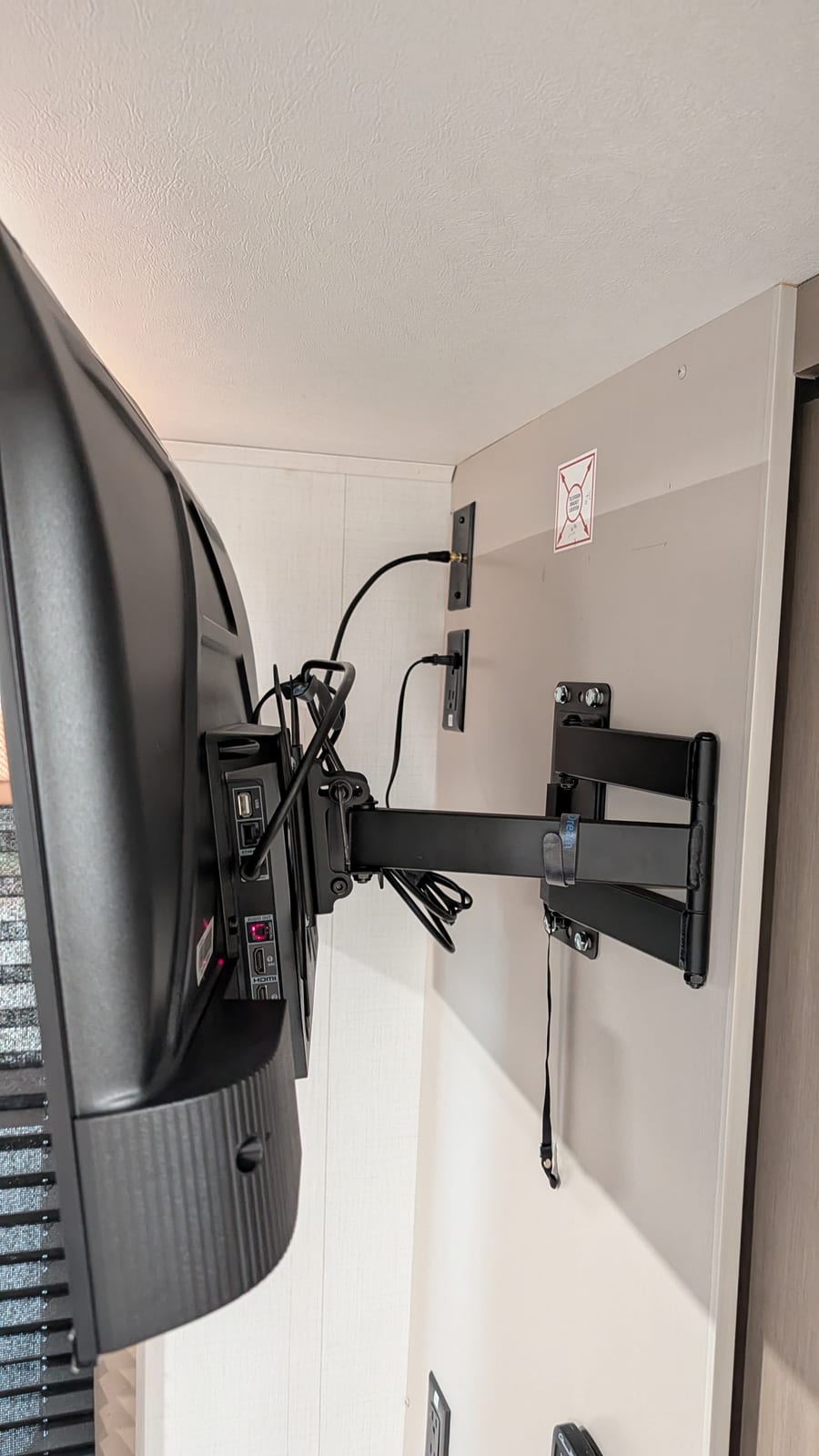 Portrait side view looking along the wall at the fully extended swing arm holding the TV, with the coax and power cables plugged into the wall jacks above the mount plate.