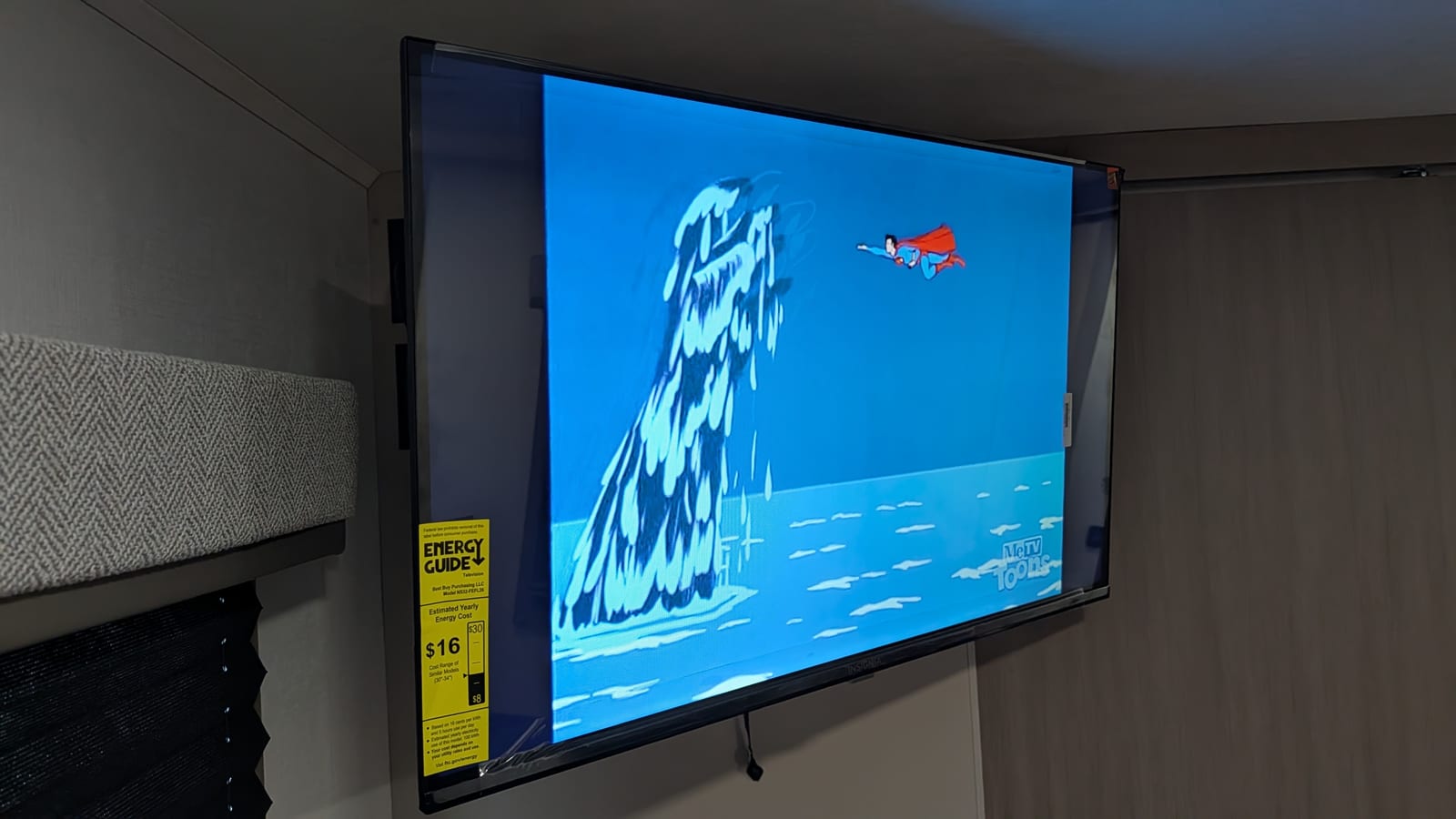 The new TV angled out on its arm, showing a classic animated Superman flying over the ocean past a large splash of water, with the MeTV Toons logo in the corner and a yellow Energy Guide sticker still on the screen.